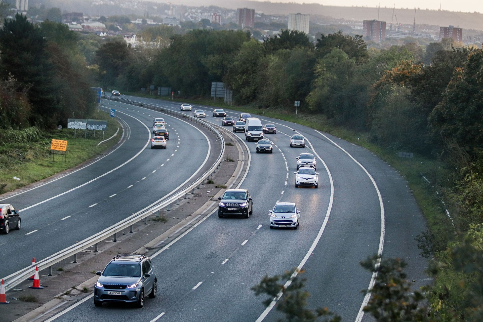 Cars driving on a curving multi-lane highway bordered by trees at dusk