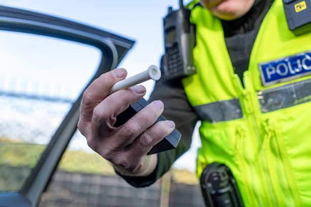 Police officer in yellow reflective jacket holding a breathalyzer beside an open car door